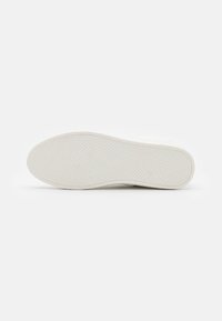 Hvit sneakersåle med teksturert gummi, med et diamantmønster for grep og en glatt overflate langs kantene. Minimalistisk design.