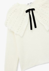 Maglione bianco con tessuto a coste, caratterizzato da un giromanica lavorato a maglia con motivo a chevron decorato con piccole perle e un fiocco di velluto nero al centro.