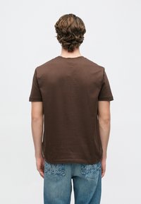 Καφέ κοντομάνικη μπλούζα με στρογγυλή λαιμόκοψη, με μαλακή υφή και άνετη γραμμή, σε συνδυασμό με μπλε τζιν που έχει διακοσμητικά ράμματα.