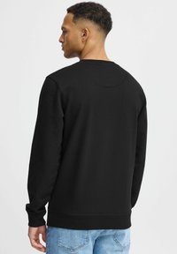 Zwarte sweatshirt met lange mouwen, ronde halslijn en geribbelde manchetten. De textuur van de stof is glad, gecombineerd met lichtblauwe spijkerbroek.