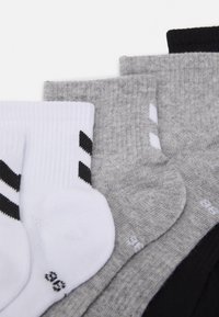 Calcetines deportivos de algodón en blanco, gris claro, gris oscuro y negro, con texturas y rayas variadas en el par blanco.