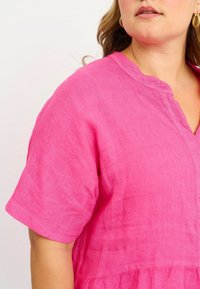 Vestito in lino rosa brillante con maniche corte, scollatura a V e fondo arricciato. Tessuto morbido con dettagli di cucitura delicati.