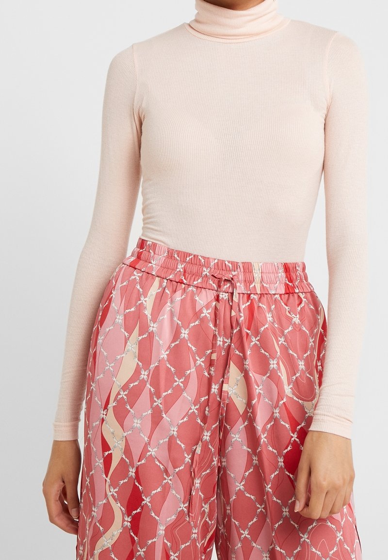 Helles rosa geripptes Rollkragenoberteil kombiniert mit lockeren, gemusterten Hosen, die ein rotes und blassrosa geometrisches Design und einen elastischen Bund haben.