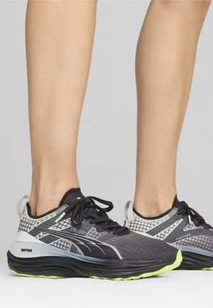 Jooksujalatsid, mis sisaldavad võrkmaterjali ja sünteetilisi elemente, musta ja halli värvipaleti, paksu talla roheliste aktsentidega ning nöörimisega disaini.