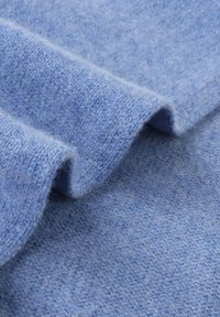 Tissu bleu doux avec une texture subtile, présentant des plis qui révèlent une surface lisse et une finition légèrement duveteuse.