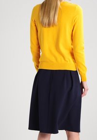 Gul stickad tröja med rund halsringning kombinerad med en marinblå A-linjekjol, med veck och en slät textur.