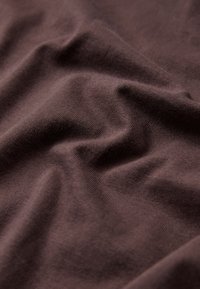 Μαλακό καφέ ύφασμα με απαλά πτυχώσεις και ζάρες, που εμφανίζει λεία και λεπτή πλεκτή υφή.