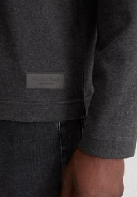 Ciemnoszara bluza z prążkowaną fakturą. Zawiera prostokątną metkę z logo "Marc O'Polo". Mankiety i dół wykończone są przeszyciami.