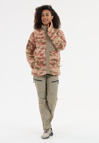 Fleecejacka i rosa och beige kamouflage-mönster med dragkedja fram, tillsammans med beiga byxor med dragkedjefickor och avsmalnande ben.