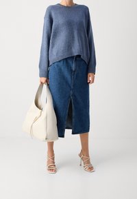 Niebieski sweter dzianinowy, spódnica z wysokim stanem z denimu z rozcięciem z przodu, beżowa torebka na ramię i beżowe sandały na wysokim obcasie z paskami.