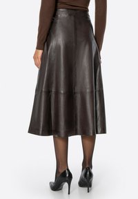 Bruine leren midi-rok met een uitlopende pasvorm, zichtbare naden en een gladde, glanzende textuur, gecombineerd met zwarte hoge hakken.