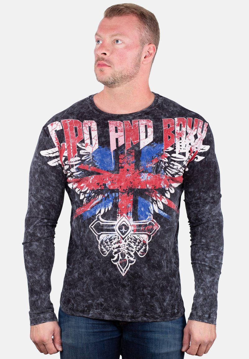 Schwarzes Langarm-T-Shirt mit Grafik, das ein beschädigtes Union Jack-Design mit roten und blauen Akzenten sowie kräftigem weißen Text zeigt.