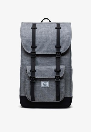 Sac à dos en tissu gris avec des accents noirs, fermeture à rabat, bretelles réglables, poche avant et patch de logo signature en bas.