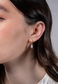 Goldfarbene Ohrhänger mit einem strukturierten Ring und einem lavendelfarbenen Edelstein in Blumenform, die eine polierte Oberfläche und ein elegantes Design zeigen.