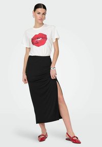 Witte T-shirt met grafisch ontwerp van rode lippen, gecombineerd met een zwarte maxi-rok met een zijsplit. Draag het met rode slingback schoenen met stippen.
