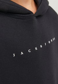 Fekete kapucnis pulóver, pamutból készült, húzózsinórral és egy modern betűtípussal a mellkasán elhelyezett "JACK & JONES" fehér logóval.