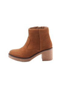 Bottine en daim marron avec un bout arrondi, sans lacets, design avec découpe sur le côté et un talon en bloc texturé. Doublure intérieure lisse visible.