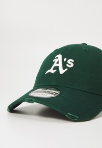 Grønn baseballcaps laget av bomull, med en hvit brodert "A's"-logo, en justerbar stropp, og en noe slitt brem.