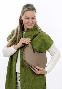 Borsa a spalla in pelle marrone chiaro con forma curvata e dettagli neri, caratterizzata da una superficie testurizzata e una tracolla corta, tenuta da una persona in un indumento verde.