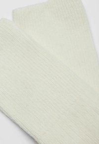Crème-kleurige gebreide sokken met een geribbeld textuur, gemaakt van een zachte, pluizige stof en een naadloze teen voor comfort.