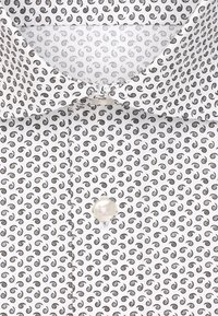 Witte shirt met een herhalend zwart spiraalpatroon, voorzien van een klassieke kraag en een knoopsluiting aan de voorkant. Gladde stoftextuur.