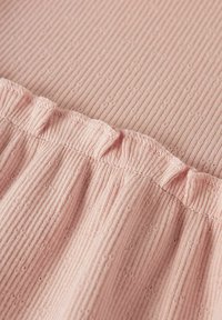 Tessuto rosa chiaro con una texture a righe e piccole macchie a motivo. Il bordo superiore ha un orlo arricciato cucito con filo coordinato.