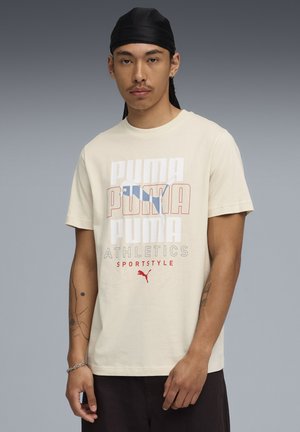 Lys beige bomulds t-shirt med et flerfarvet Puma logo design, korte ærmer og en løs pasform. Klassisk crew-udskæring.