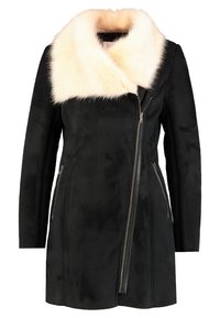 Cappotto in suede nero con collo in pelliccia sintetica bianca, chiusura con zip asimmetrica, tasche laterali e design snello. Texture complessivamente liscia.