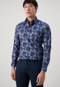 Långärmad skjorta i blått tyg med röda och teal blommönster. Knapp-down krage och figursydd design med en mjuk textur.