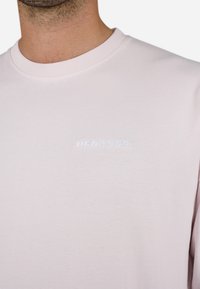 Light pink long-sleeve t-shirt made of soft cotton, featuring a crew neckline and subtle embroidered branding in white on the chest.
