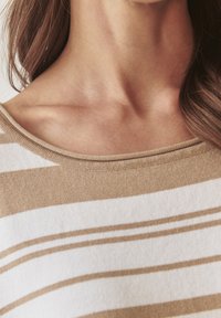 Un haut en tricot doux avec un col large, orné de rayures horizontales blanches et beiges alternées. La texture semble lisse et légère.