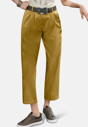 Pantalons plissés jaunes avec une finition lisse, dotés d'une large ceinture et d'une ceinture marron, associés à des baskets grises.