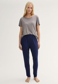 T-shirt grigia a maniche corte abbinata a pantaloni della tuta aderenti blu navy. Tessuto morbido, vestibilità rilassata e vita elastica sui pantaloni.