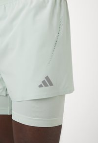Pantalones cortos deportivos de color verde claro con un diseño transpirable, cinturilla elástica y acentos de logo en gris. La capa interior tiene un acabado texturizado.