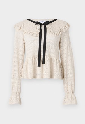 Top in pizzo beige con colletto arricciato e maniche lunghe. Presenta un fiocco nero all'aita e un'orlo a peplo svasato.