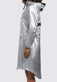 Srebrny wodoodporny płaszcz przeciwdeszczowy z kapturem, elastycznymi mankietami i przedłużonym tyłem. Posiada gładką, połyskliwą teksturę oraz kieszenie z przodu. Zawiera czarne akcenty.