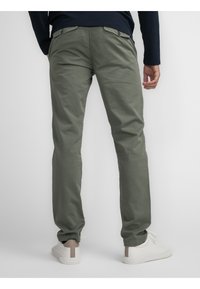 Green cotton trousers with a tapered fit, featuring two back pockets and a smooth texture. Paired with white sneakers.