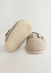 Chaussons en feutre gris clair avec une forme arrondie. Équipés d'une sangle avec une boucle en laiton. Semelle en caoutchouc avec un motif en zigzag pour une meilleure adhérence.