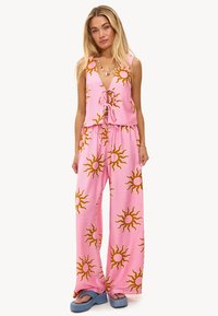 Ensemble robe d'été rose avec un haut à nouer à l'avant et un pantalon large présentant de grands motifs solaires en jaune et orange. Tissu lisse et léger.