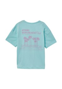 Lichtblauw katoenen t-shirt met een losse pasvorm. De voorkant heeft een roze grafisch ontwerp met palmbomen en de tekst "ATAMI SUN BEACH Club". Korte mouwen.