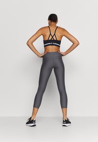 Musta urheiluliivi ristikkäisillä selkäremmeillä, harmaat mid-rise-housut ja mustat lenkkarit. Sileä ja istuva kangas, jossa hienovaraiset kuviot.