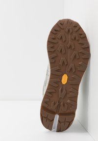 Brun gummisål med dybt mønster og Vibram-logo. Overdelen er lavet af lys grå mesh og syntetiske materialer, designet til greb.