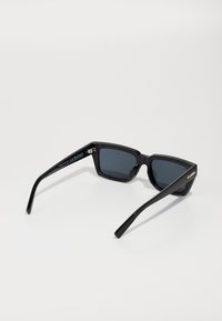 Ochelari de soare dreptunghiulari negri cu lentile gri, rame din plastic groase și brațe elegante cu accente metalice și branding pe interior.