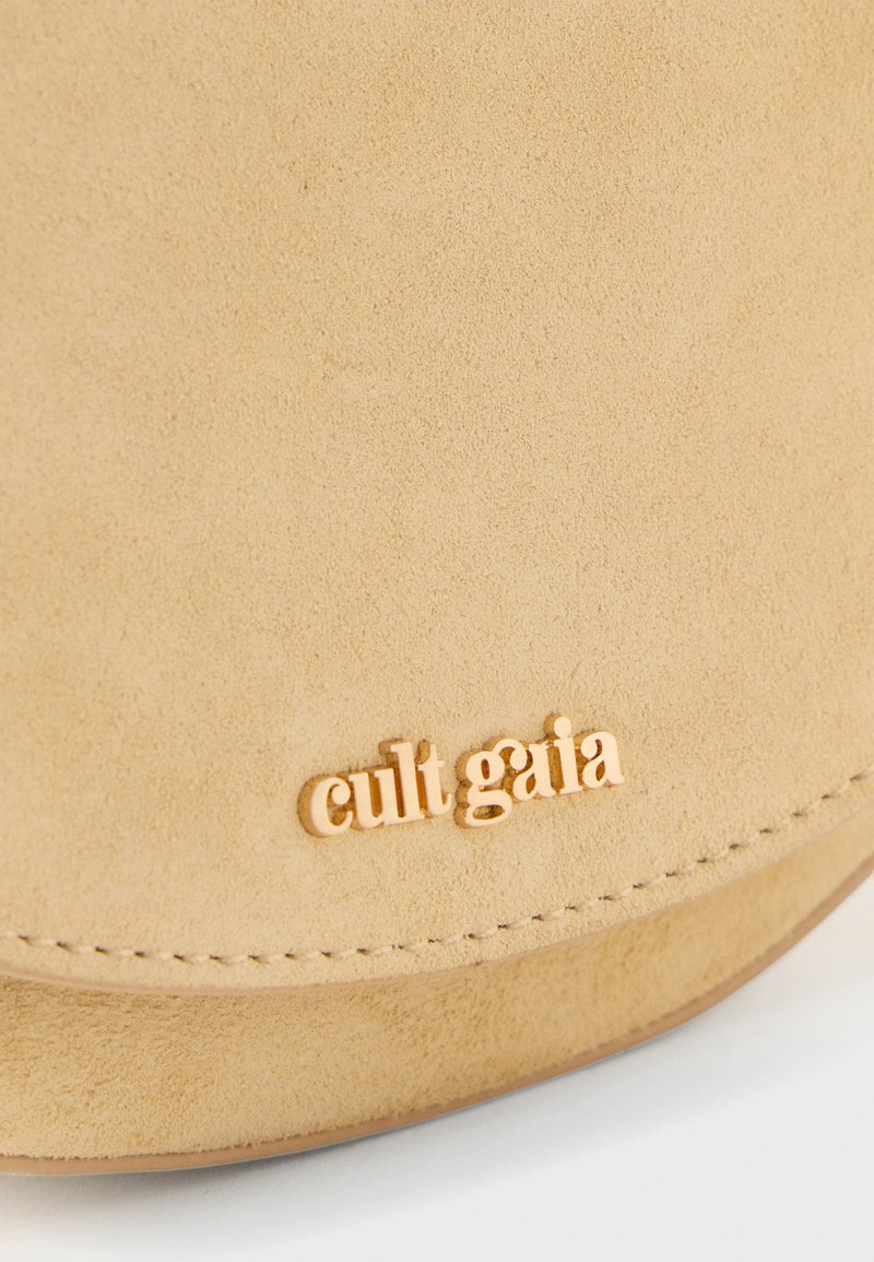 Beige suede bag with a curved shape, featuring a gold-tone "cult gaia" logo, smooth texture, and clean stitched edges.