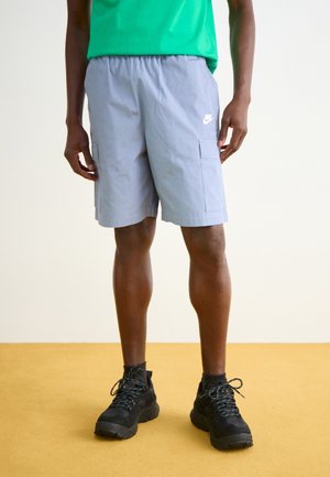 Pantalones cortos de carga grises con cinturilla elástica, que cuentan con dos bolsillos laterales y un pequeño logo blanco, combinados con zapatos de senderismo negros.