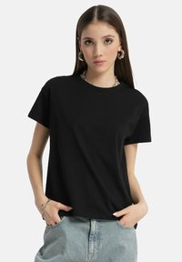 Czarna bawełniana koszulka z krótkim rękawem, okrągłym dekoltem i luźnym krojem. W połączeniu z jasnoniebieskimi dżinsowymi szortami.