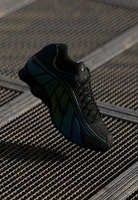 Scarpa sportiva nera con accenti verde e blu, upper in mesh texturizzato e suola ammortizzata. Presenta lacci e logo sul lato.