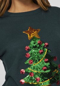 Grön tröja med design av en julgran i paljetter, prydd med röda dekorationer och en gyllene stjärna på toppen. Ribbade detaljer och rund halsringning.