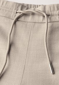 Lichtgrijze joggers met een elastische tailleband en verstelbaar trekkoord. Het materiaal heeft een fijne textuur en subtiele stikseldetails.