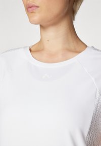 White athletic top with a smooth texture, featuring textured accents on the shoulders and a round neckline, highlighting simplicity in design.